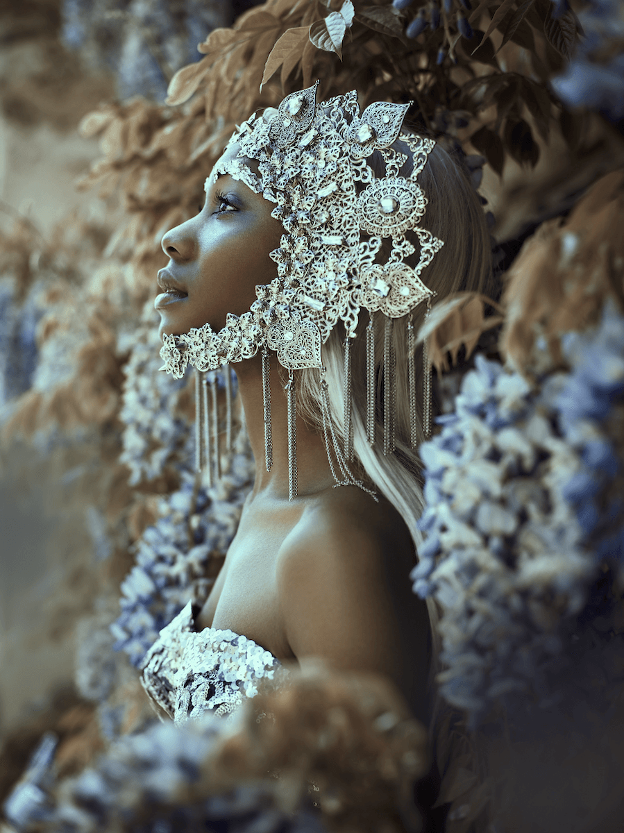 A profile shot of a woman wearing elaborate jewellery in front of flowers