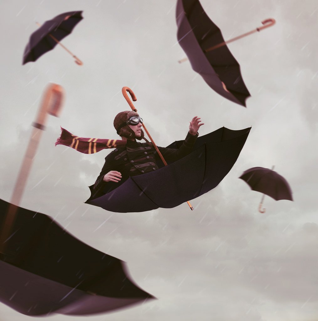 A pilot with a scarf riding an upside-down umbrella in the sky with other umbrellas falling around him