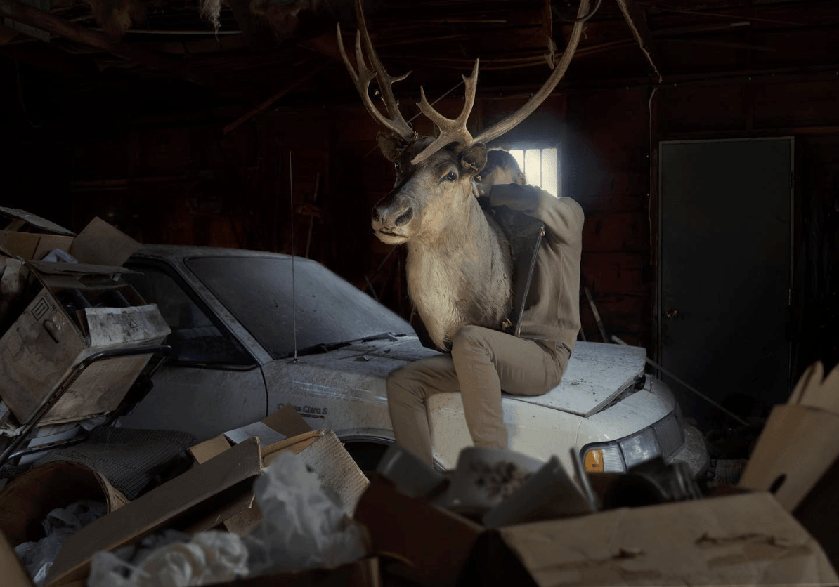 A person sitting on a car in a garage with a reindeer torso