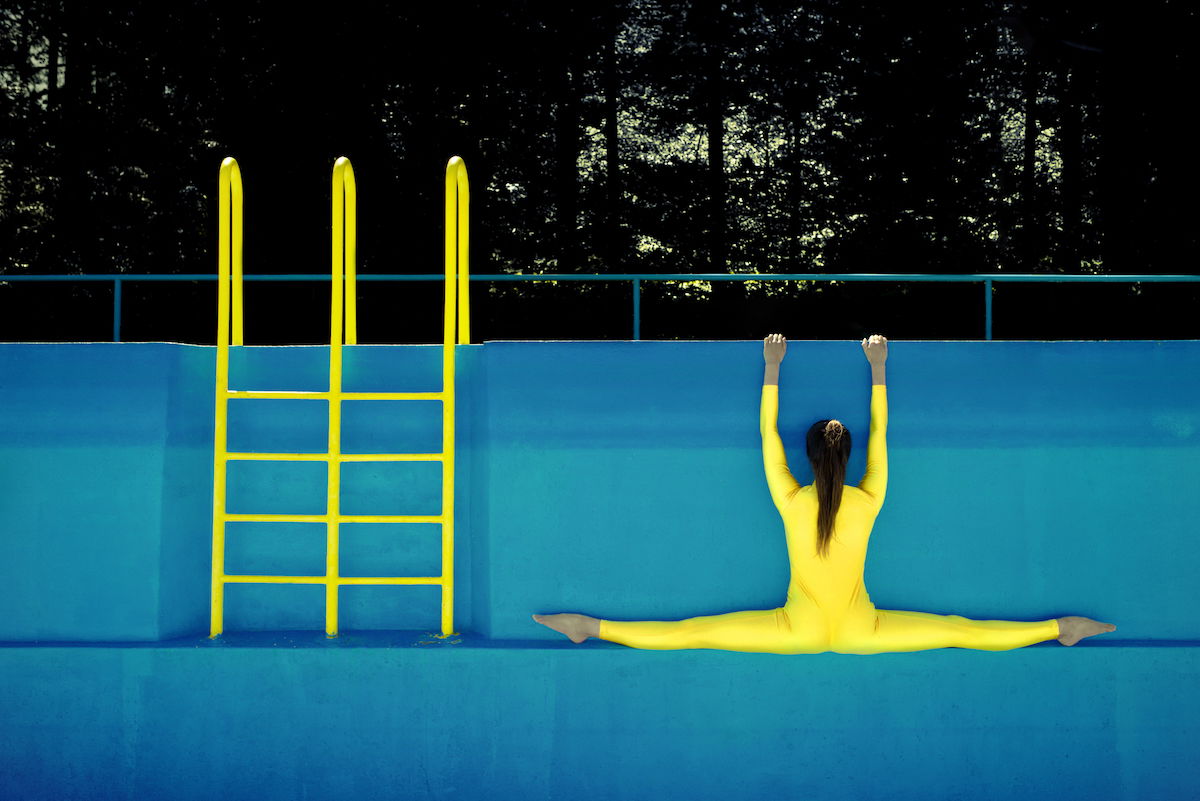 A woman doing the splits in a neon yellow jumper hanging on the side of an empty pool