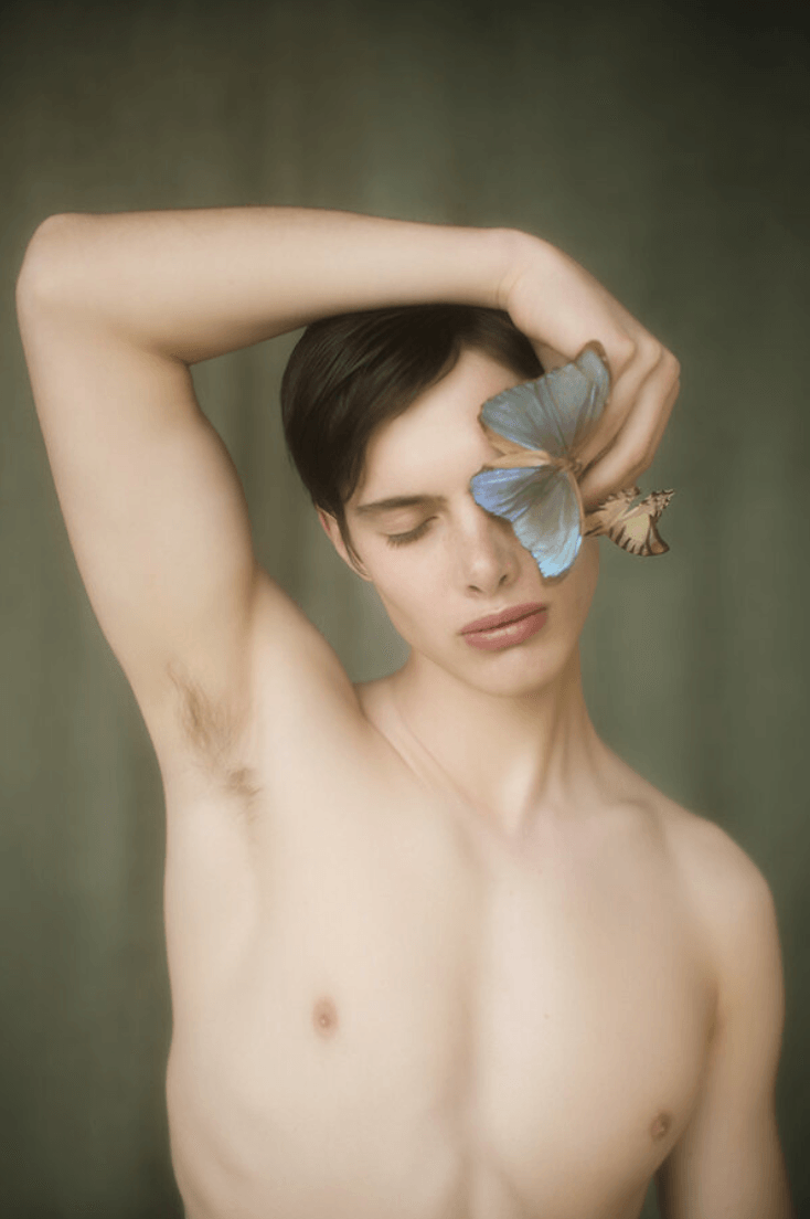 A shirtless man with his arm above his head and a butterfly on his eye