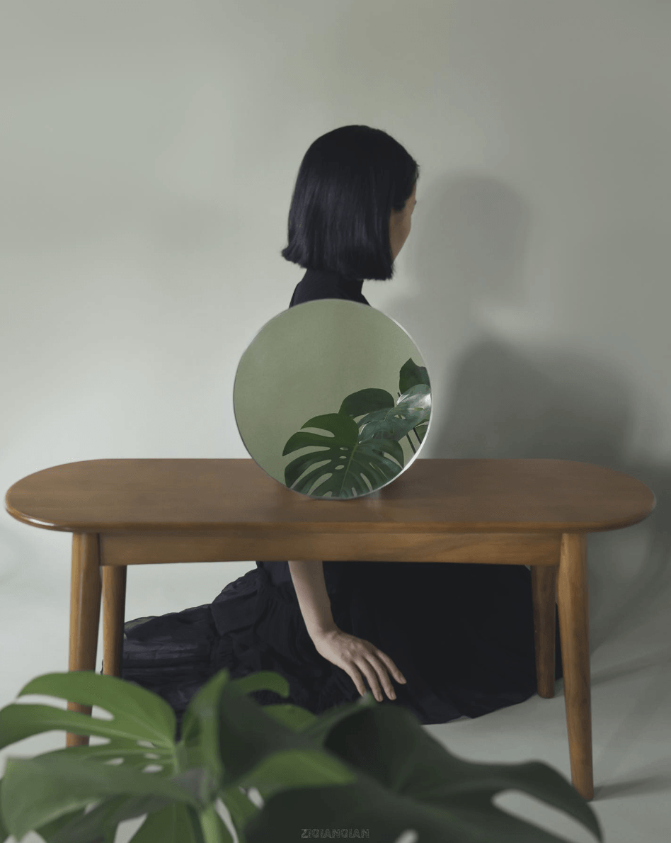 A woman posing with her back turned and a mirrored plant and table