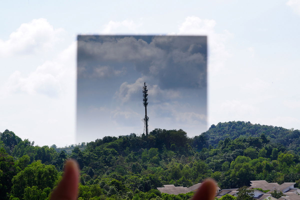 A graduated ND filter being held up to a sky and hills with trees