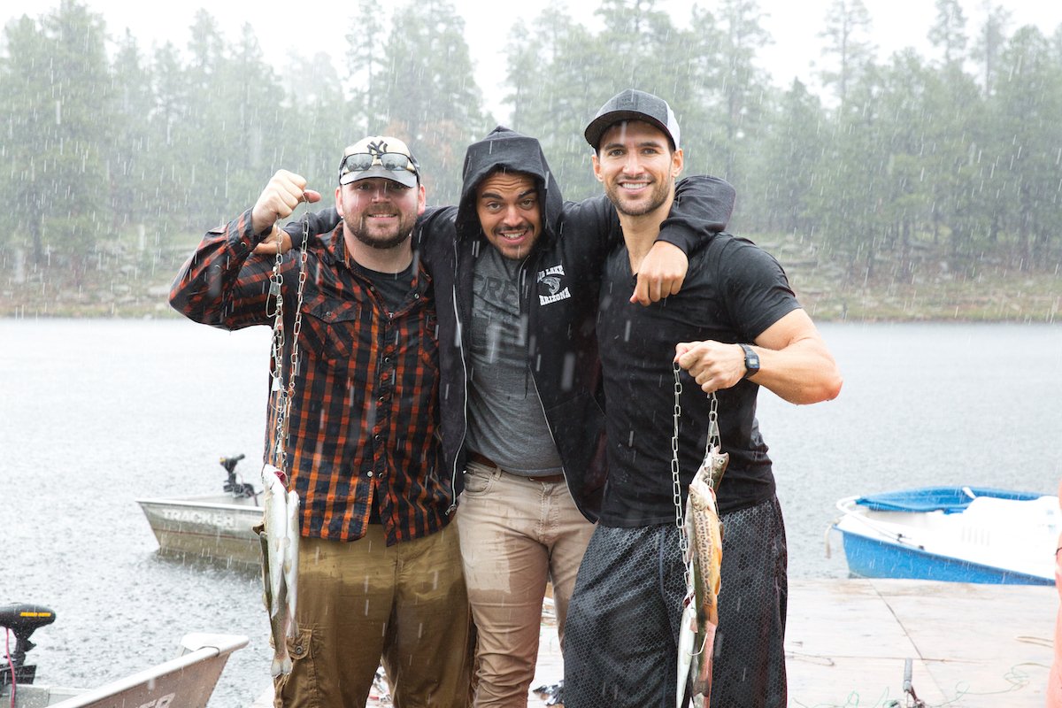 Three guys posing with fish caught by a lake