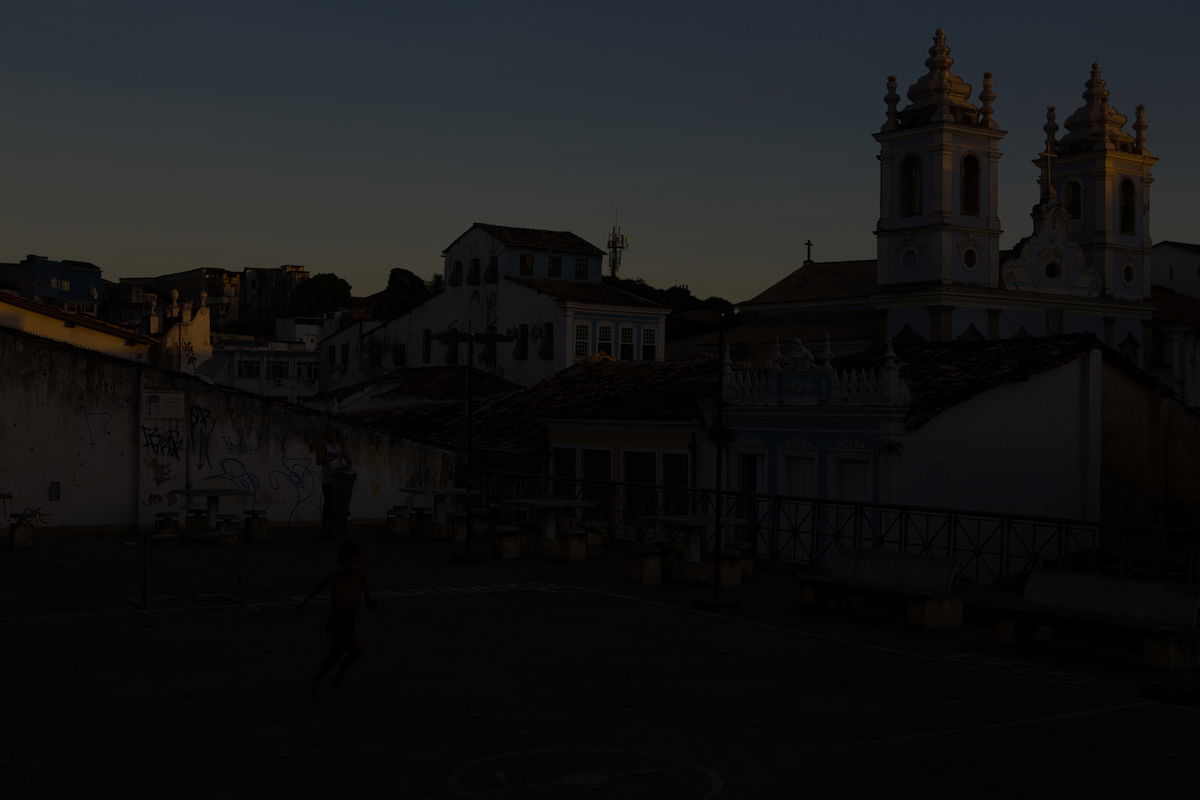 Dark, underexposed image of a boy playing in an urban court in front of a church