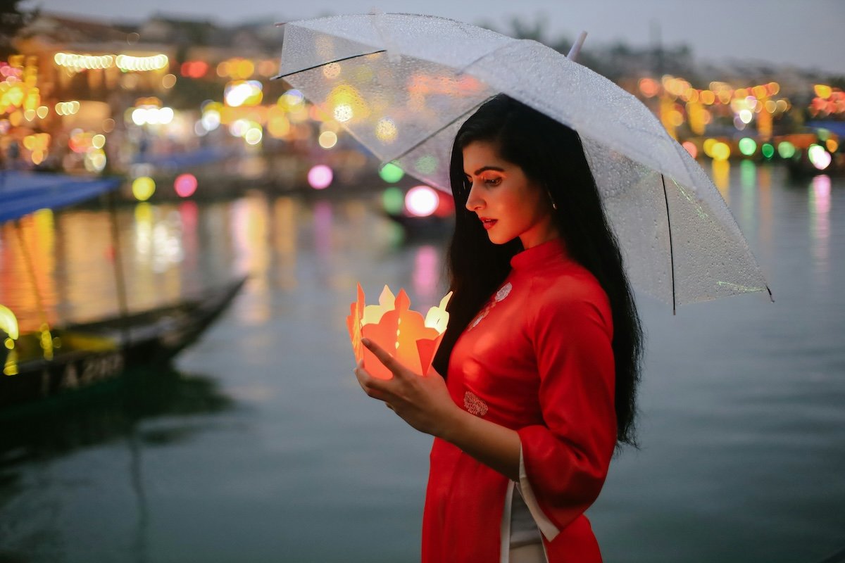 A portrait of a women holding an umbrella and small lantern with colorful light bokeh in the background caused by a wide aperture setting