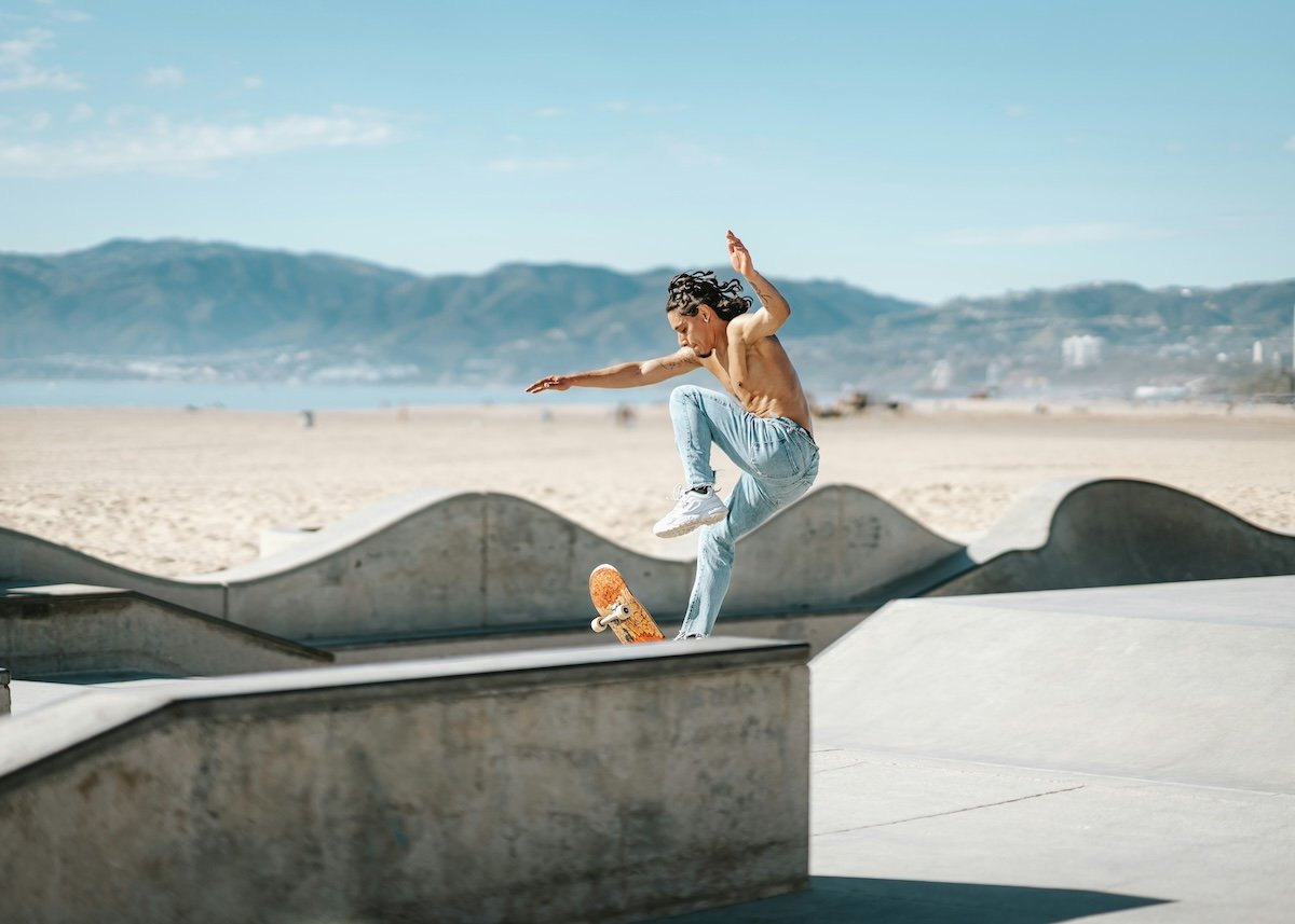 A skateboarder doing a trick at a skate park by a beach shot with a wide aperture to capture action