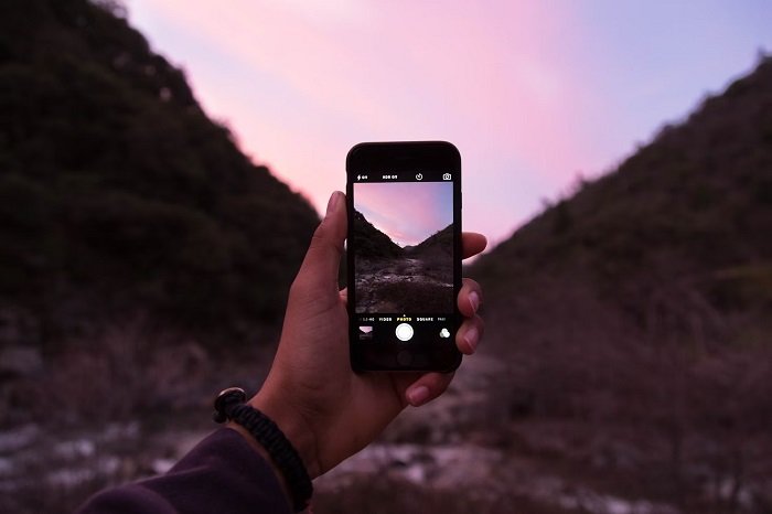 Hand holding up a smartphone that taking a picture of a landscape
