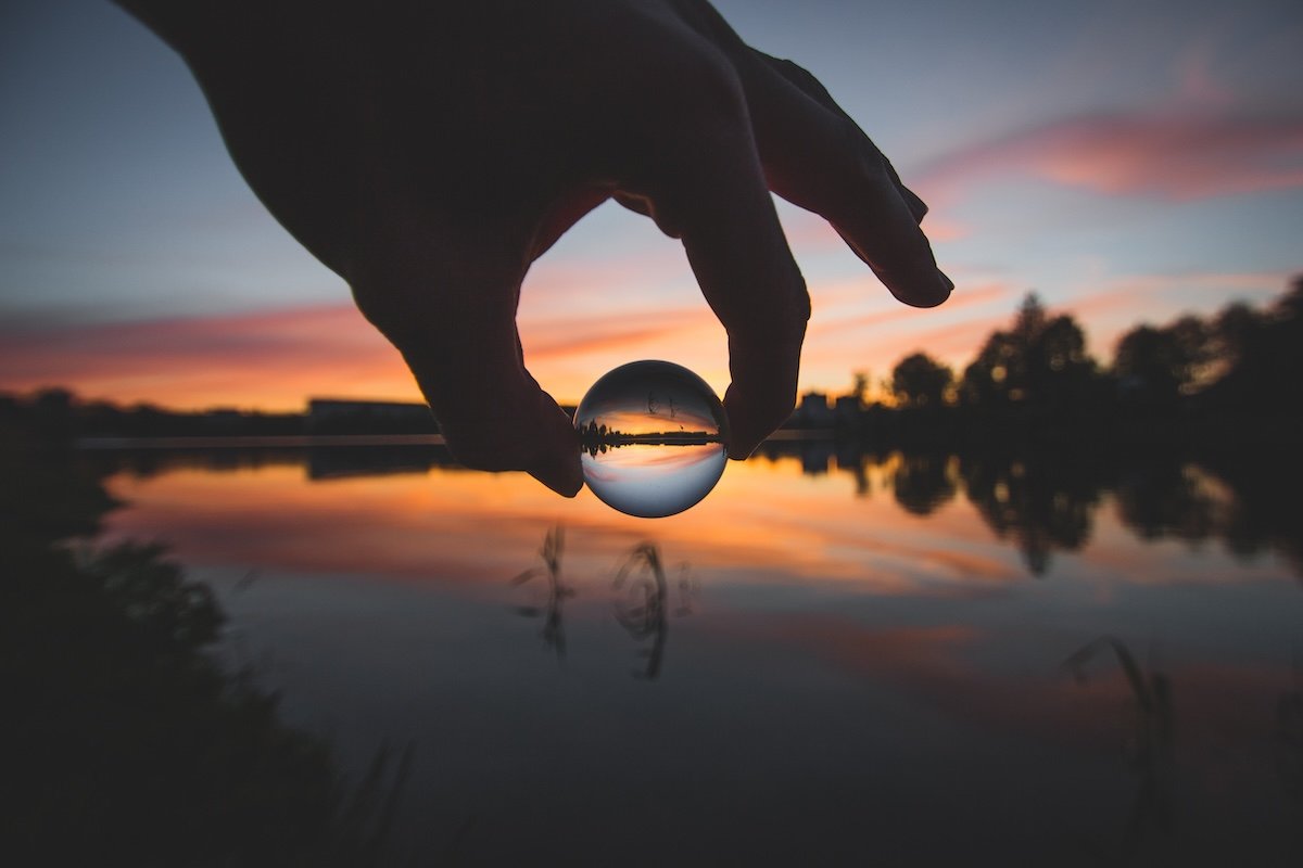 A hand holding a sphere over a lake at sunset illustrating the forced perspective photography term