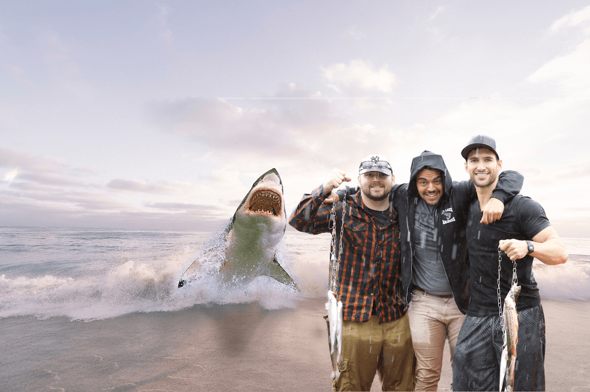 photo edit of three men after a fishing trip standing on a beach with a shark jumping at them