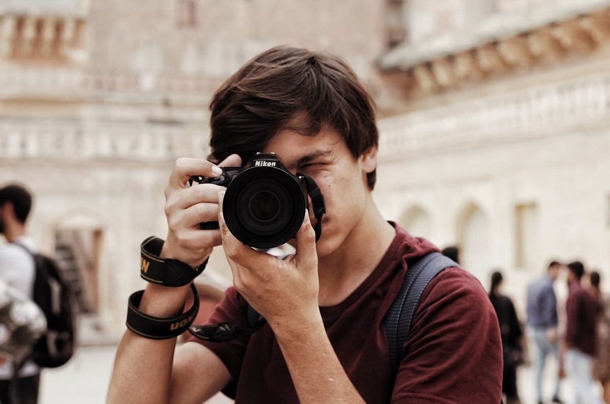 Young man holding a Nikon mirrorless camera for travel to his face in an urban space