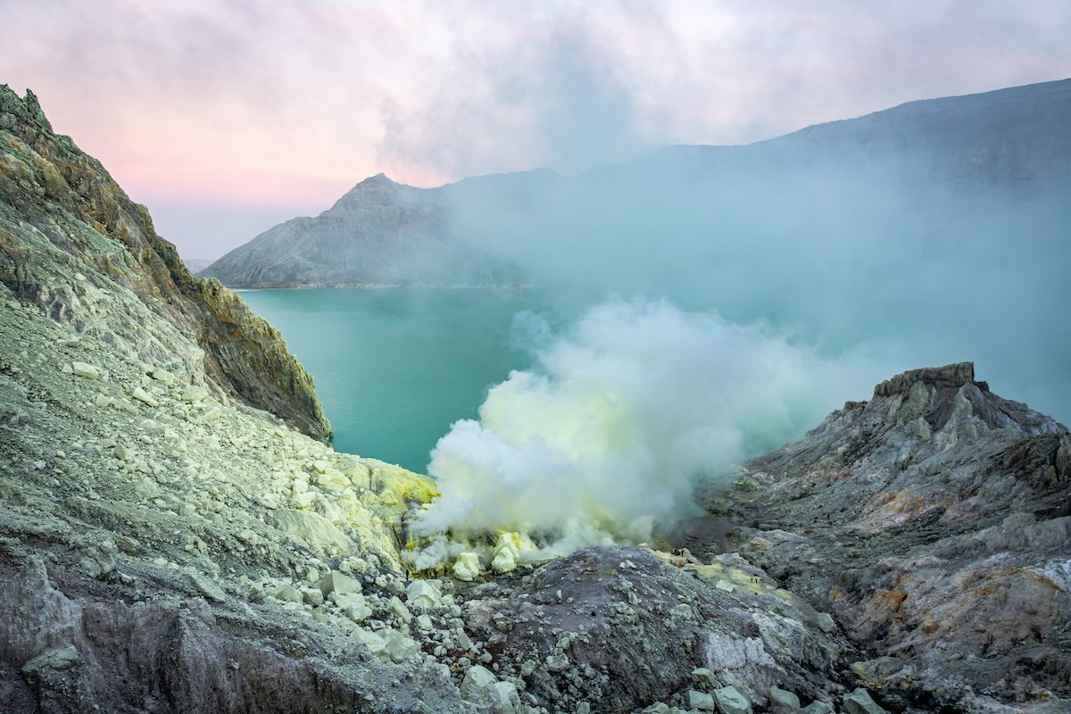 Photograph of smoke coming out of a sulphur mine with lake in the background