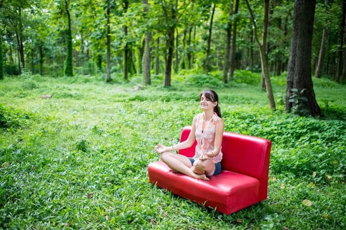 Woman sitting on a red sofa in a woodland clearing