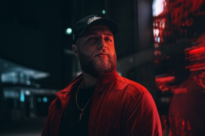 Night portrait of man with blond beard in a cap lit by a red neon light