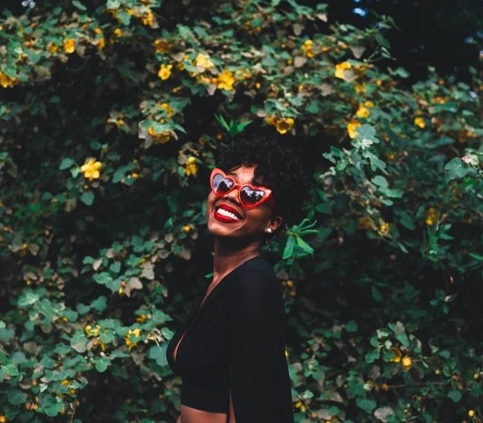 Portrait of woman in heart sunglasses in front of a tree with yellow flowers