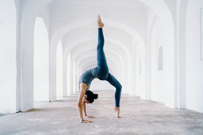 Woman doing a complex yoga pose under white arches