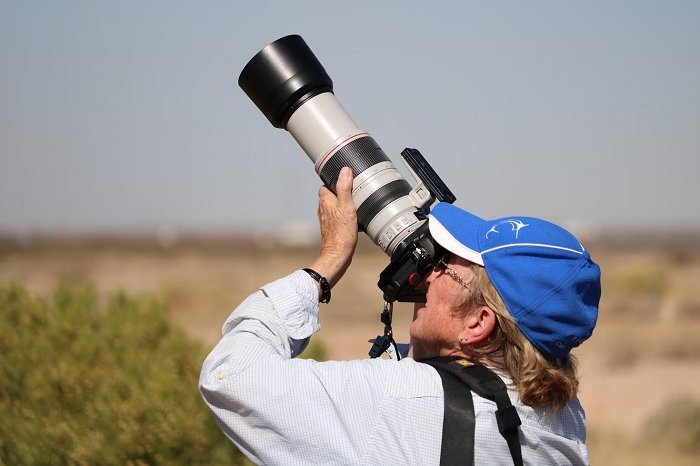 Elderly person taking a picture of a bird in the sky with a camera and telephoto lens