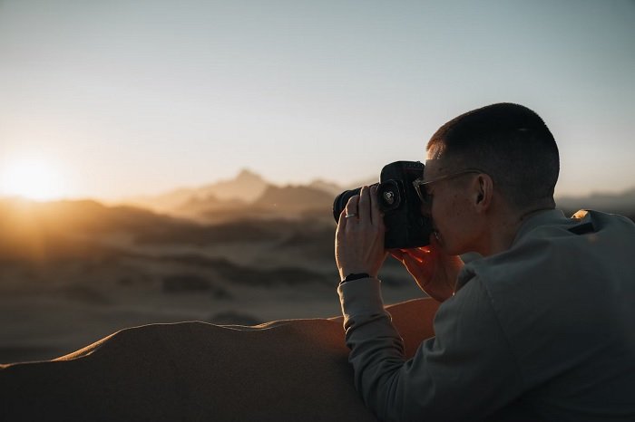 Photographer perching over the top of a sand dune