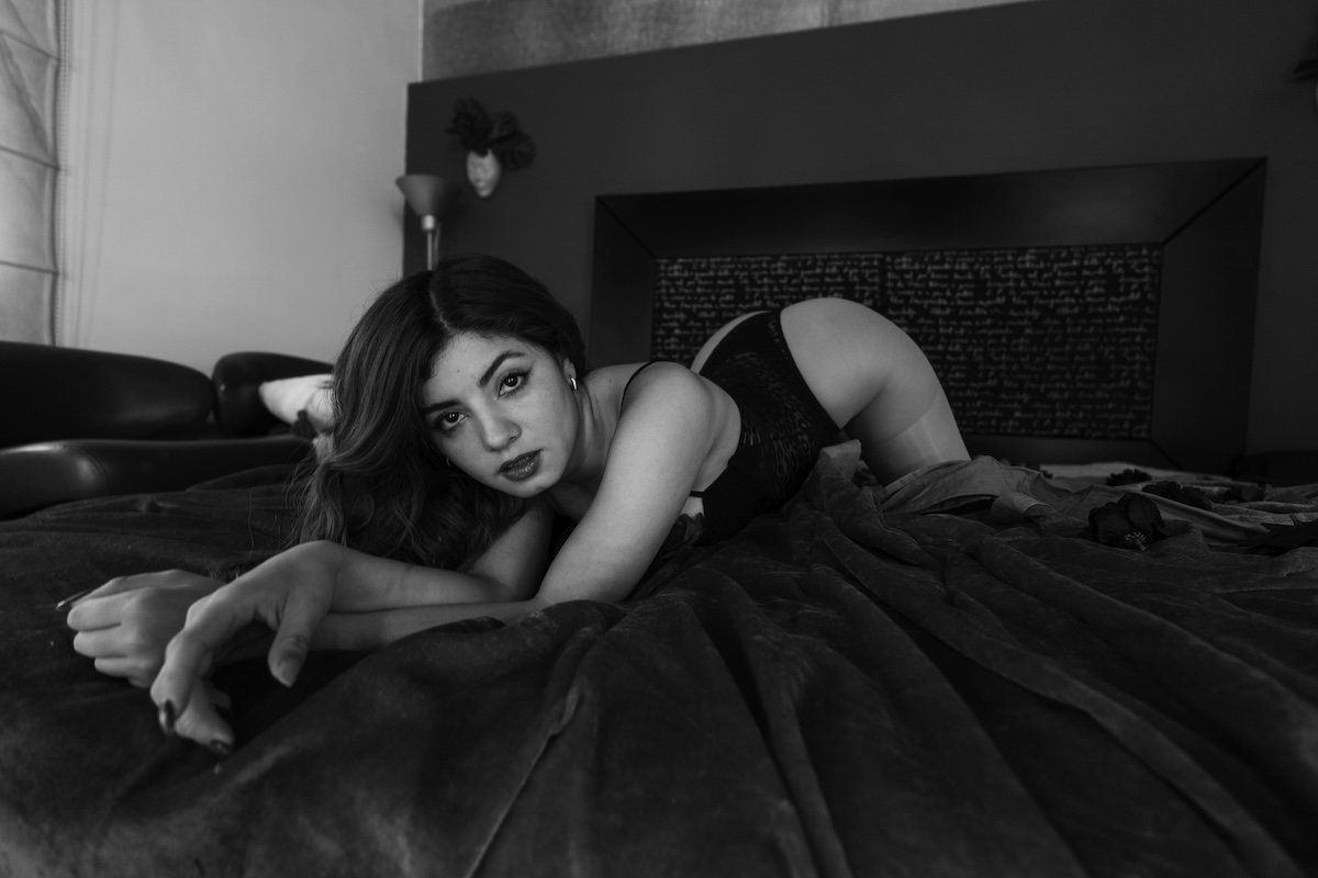 Black-and-white image of a woman posing on a bed in lingerie as an example for our boudoir photography guide