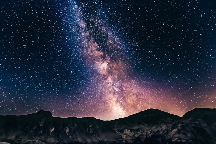 Night sky image of Milky Way cluster above rocky mountain tops