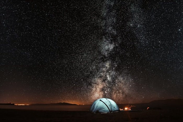 Tent lit from within below a clear night sky filled with stars for Milky Way photography