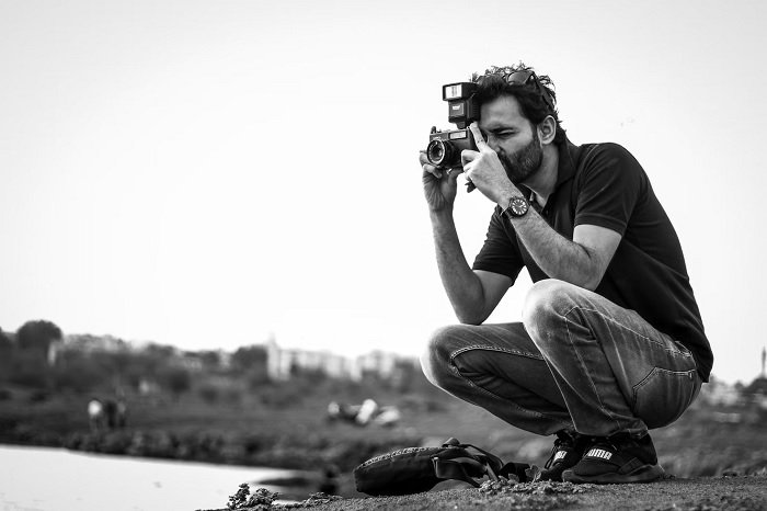 Black and white image of male photographer crouching while taking a picture
