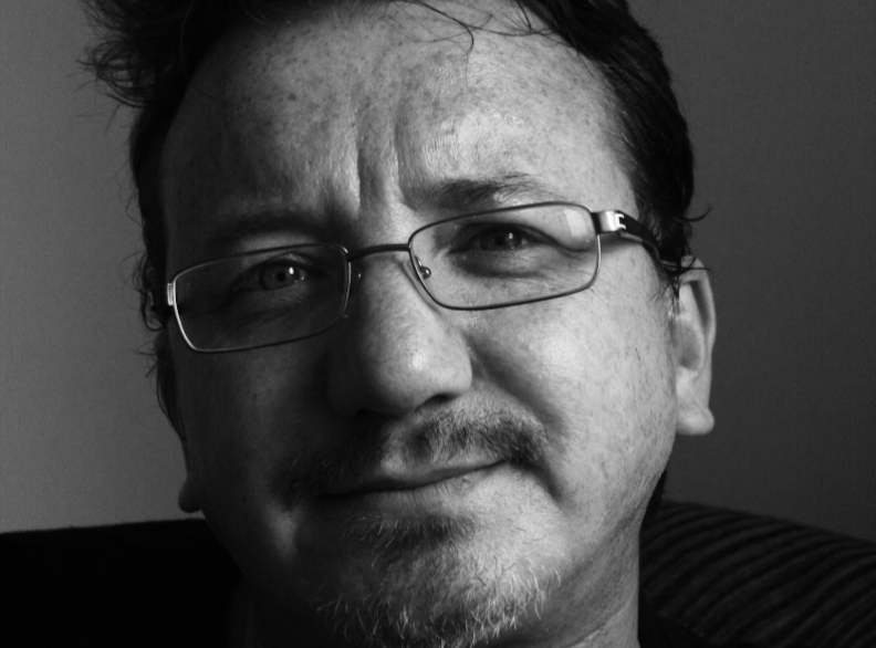 A black-and-white close-up of a man wearing glasses using split portrait lighting
