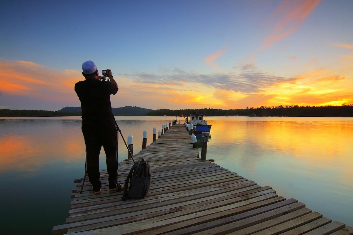 Man taking a photograph on a pier during sunset