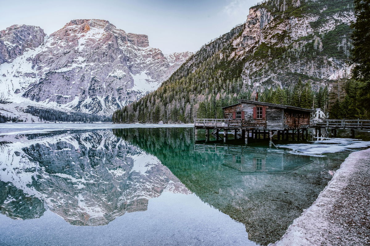 HDR image of a shack by a lake surrounded by snowy mountains