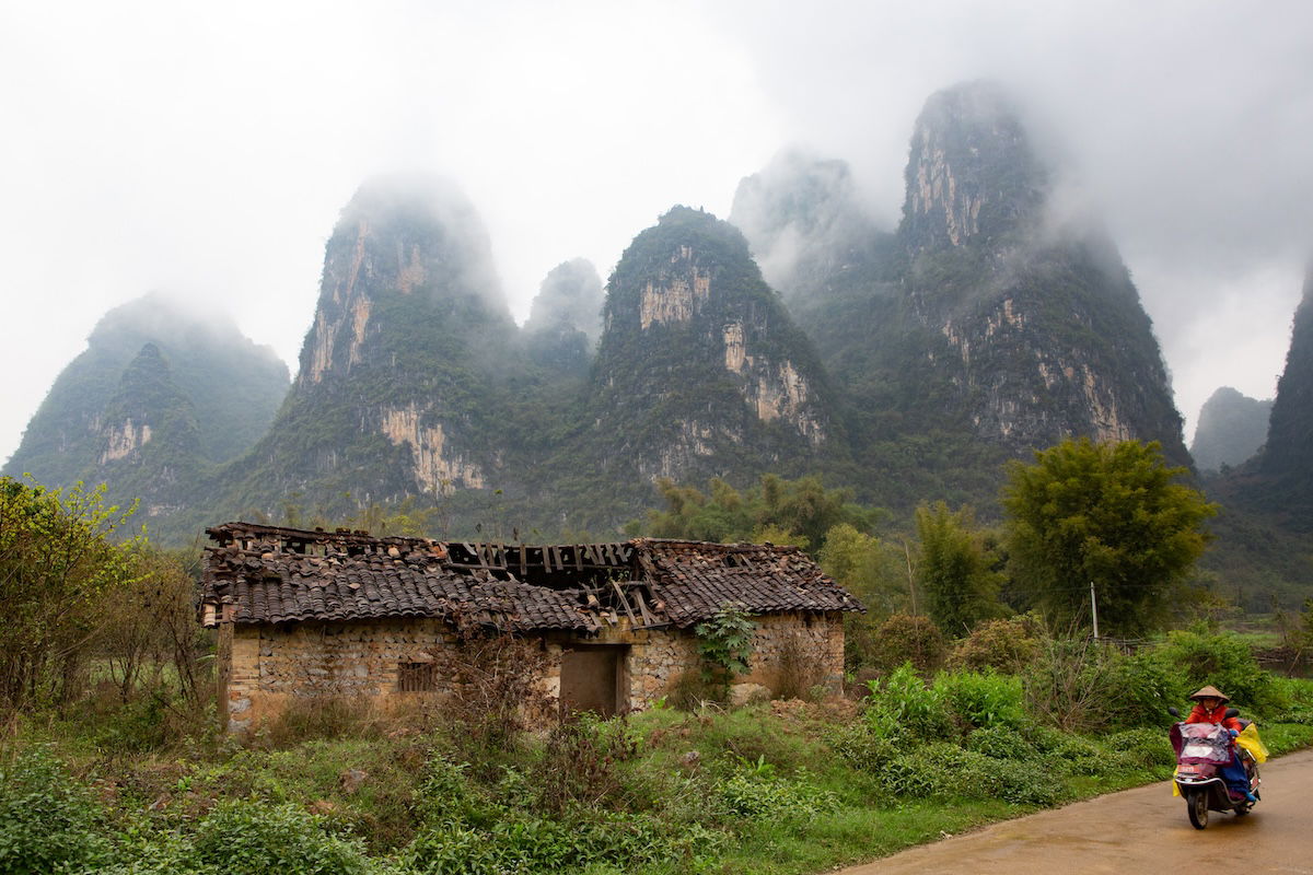 Photograph of mountains in the mist with a abandoned shed in foreground and person on a moped with dehaze