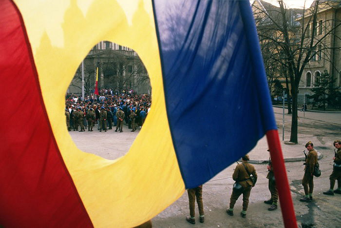 Crowd seen through hole in Romanian flag