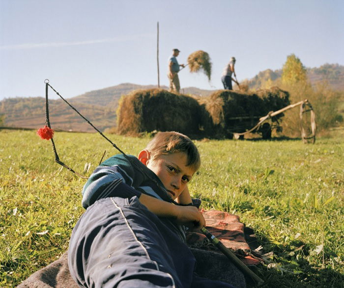 Boy laying on grass with farm workers behind