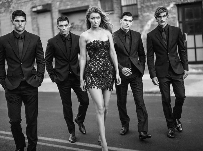 Model in dress walking in front of four men in suits