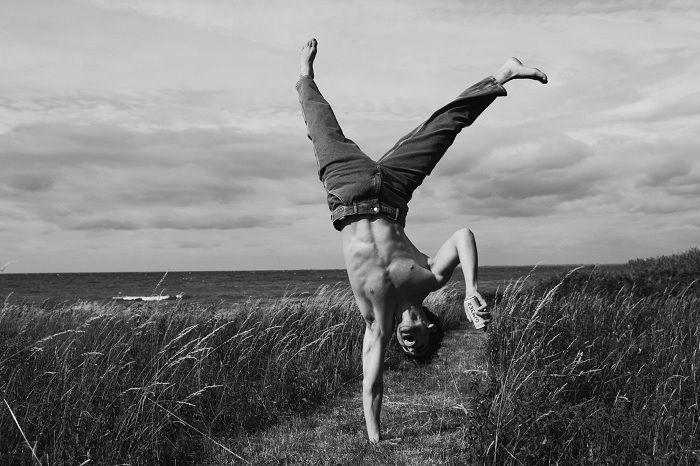 black and white image of man doing one-arm handstand in a field