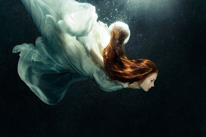 Woman with dark red hair diving underwater