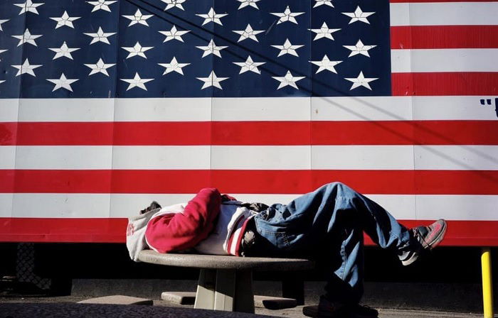 Man sleeping on a bench in front of the US flag