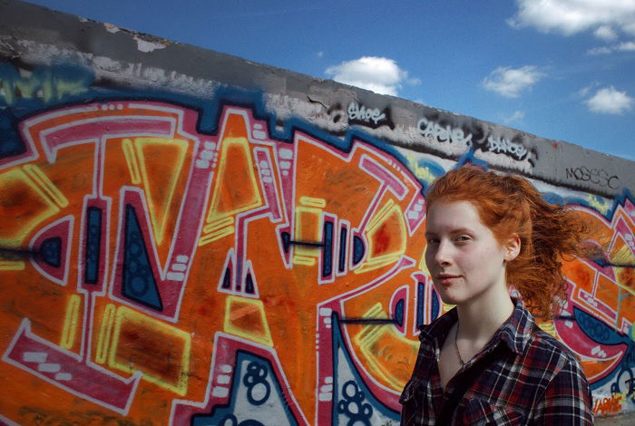Woman with red hair walking past gaffitied wall