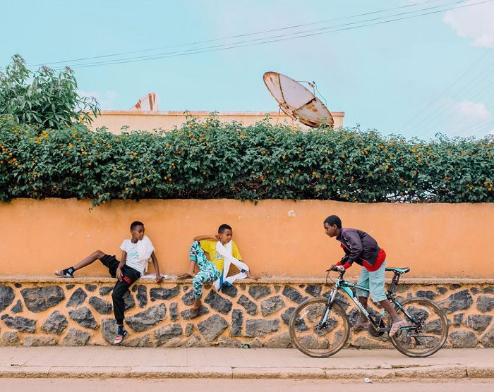 Two kids sitting on a wall with another kid riding a bike