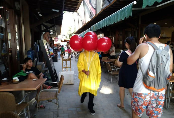 Person walking with three red balloons that cover their face