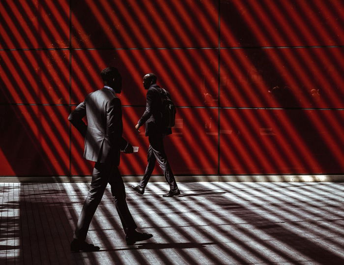 Two men walking in different direction under stripped lighting