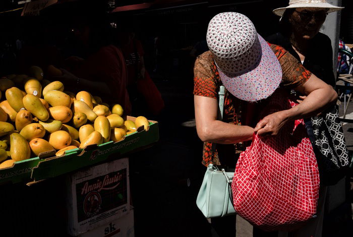 Woman in hat with head lowered next to mango stall