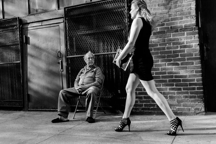 Woman in dress and heels walking past man in chair