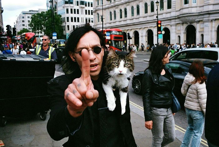 Man with cat on shoulder pointing at the camera