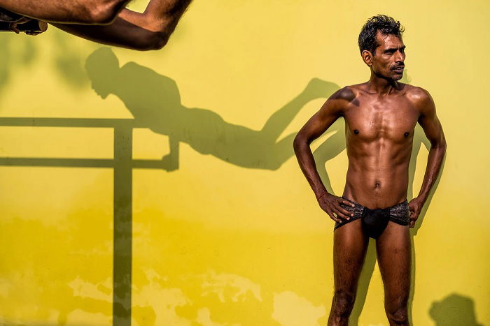Nearly naked man standing in front of a yellow wall next to shadow of another man