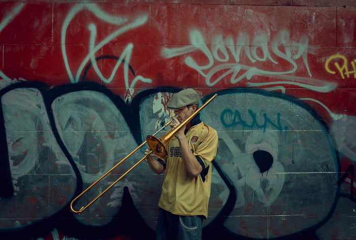 Man playing trombone next to wall with graffiti