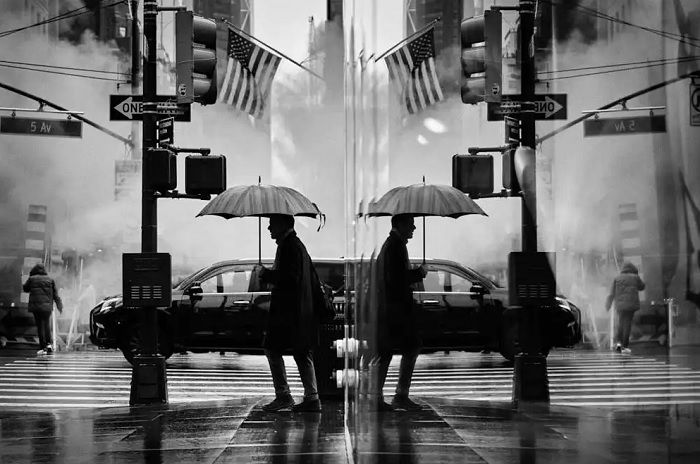 Man with umbrella seen in window reflection