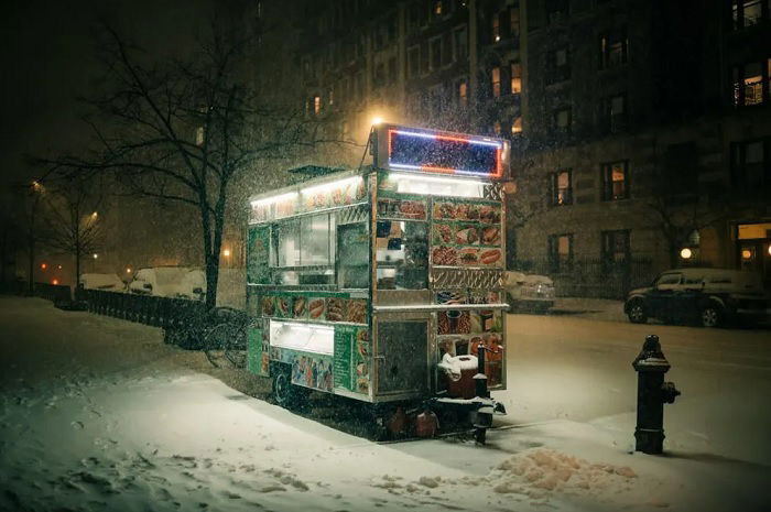 Hotdog trailer lit up in dark snowy street