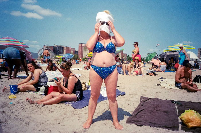 Middle-aged woman standing on a beach with towel on face