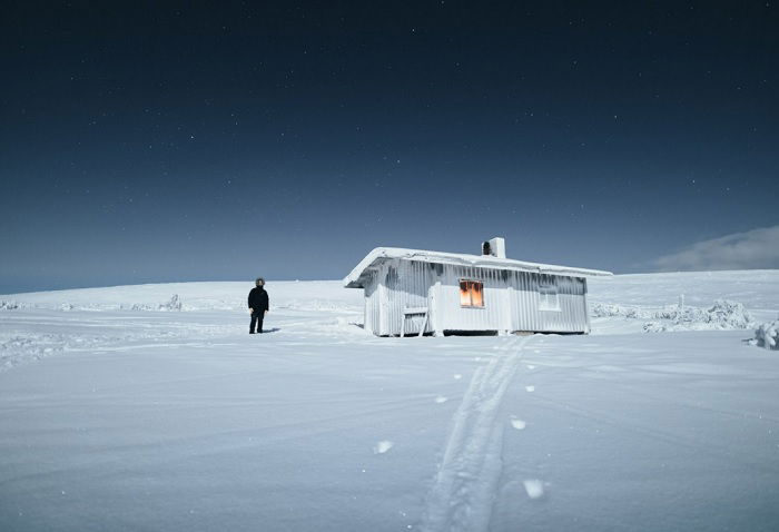 Man standing outside small cabin in snowy landscape