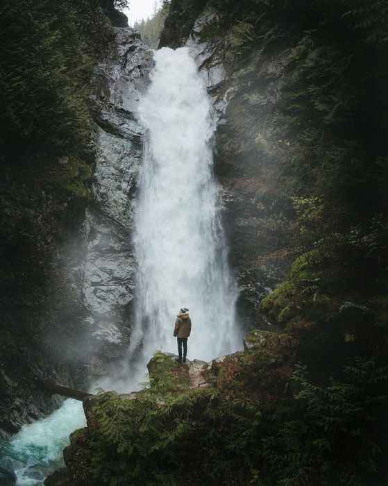 Man standing on rock at the bottom of a waterfall